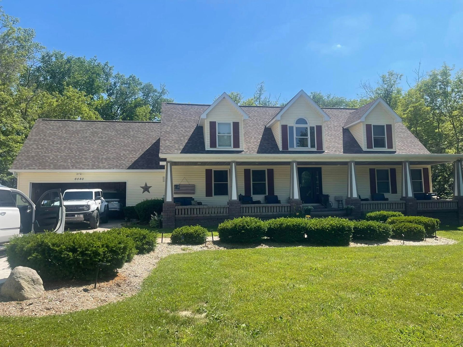 Two-story beige house with brown roof and a white SUV in the garage on a sunny day.