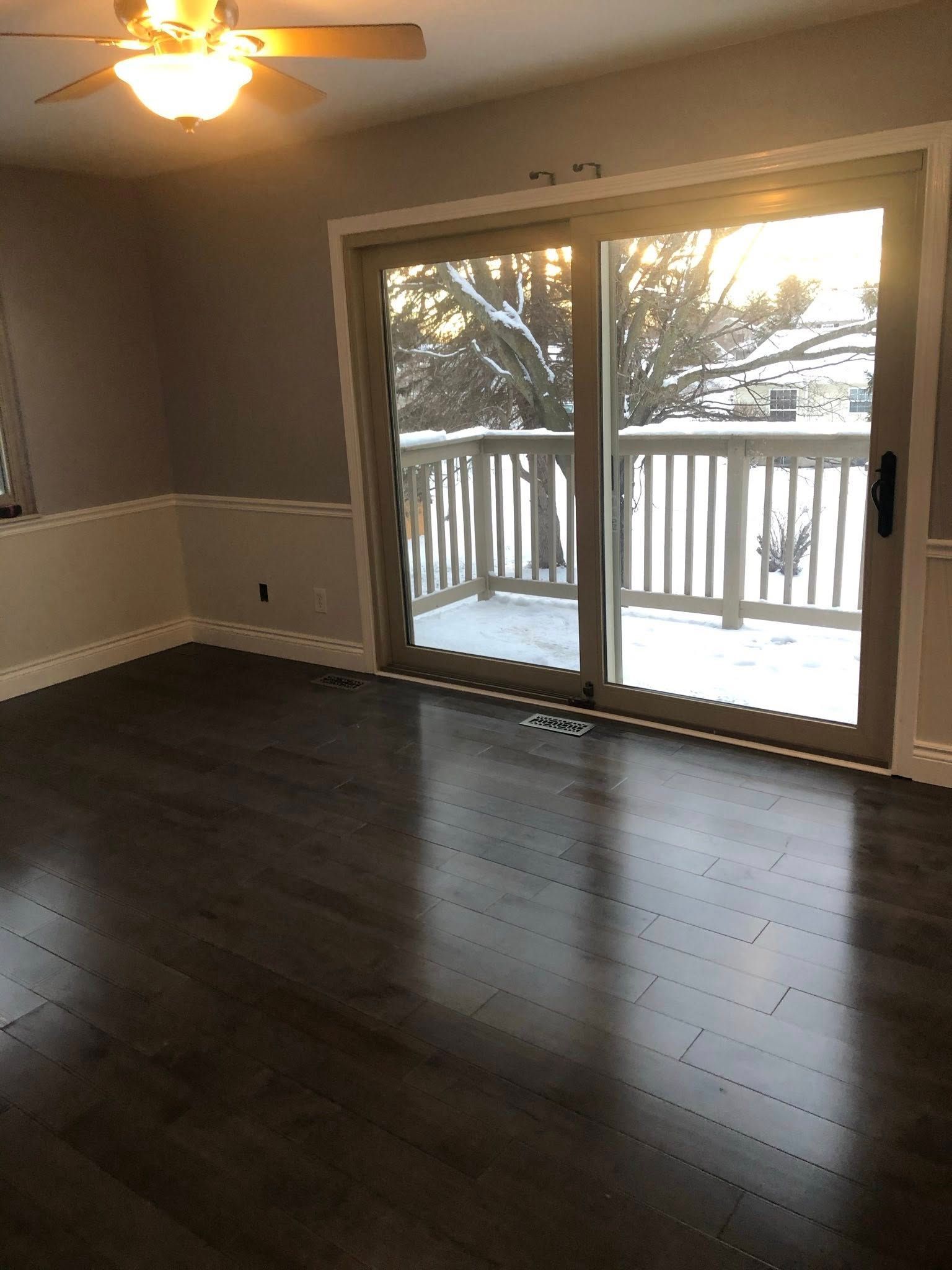 Room with wood floor, sliding glass door to snowy deck. Gray walls, white trim, ceiling fan.