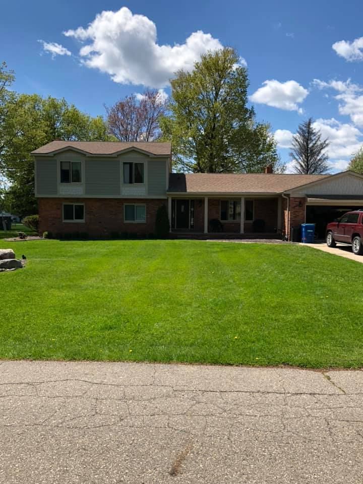 Two-story house with green siding on top, brick below, and a well-kept lawn. Blue sky with clouds.