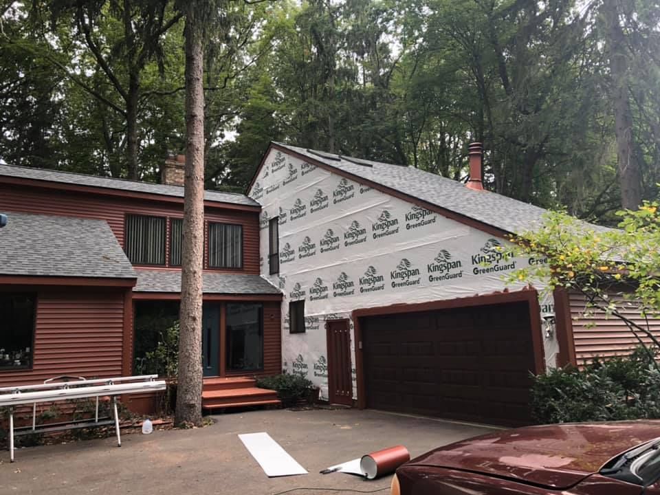 House exterior under construction, with exposed sheathing, partial roof, garage, and driveway.