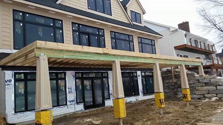 Building under construction with black framed windows, tan siding, and a wooden porch.