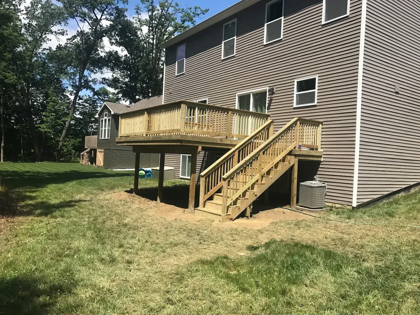 Wooden deck attached to a two-story gray house, with stairs leading down to a grassy yard.