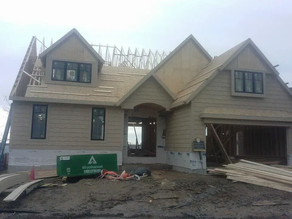 A partially constructed house with tan siding, black windows, and a garage, under a cloudy sky.