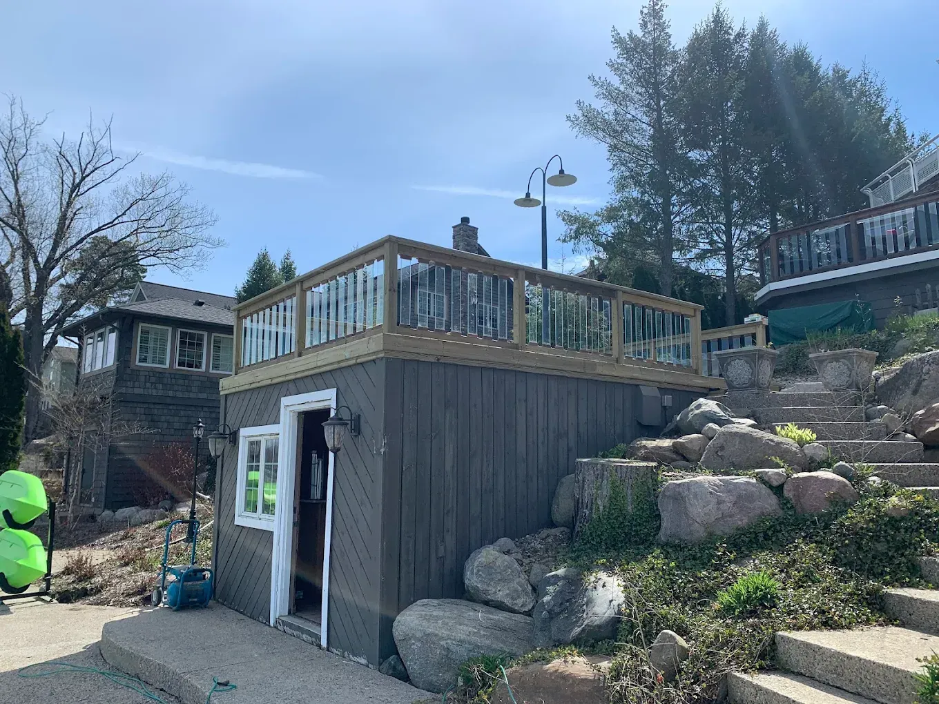 Building with a wood deck and glass railing, next to stairs and rocks.