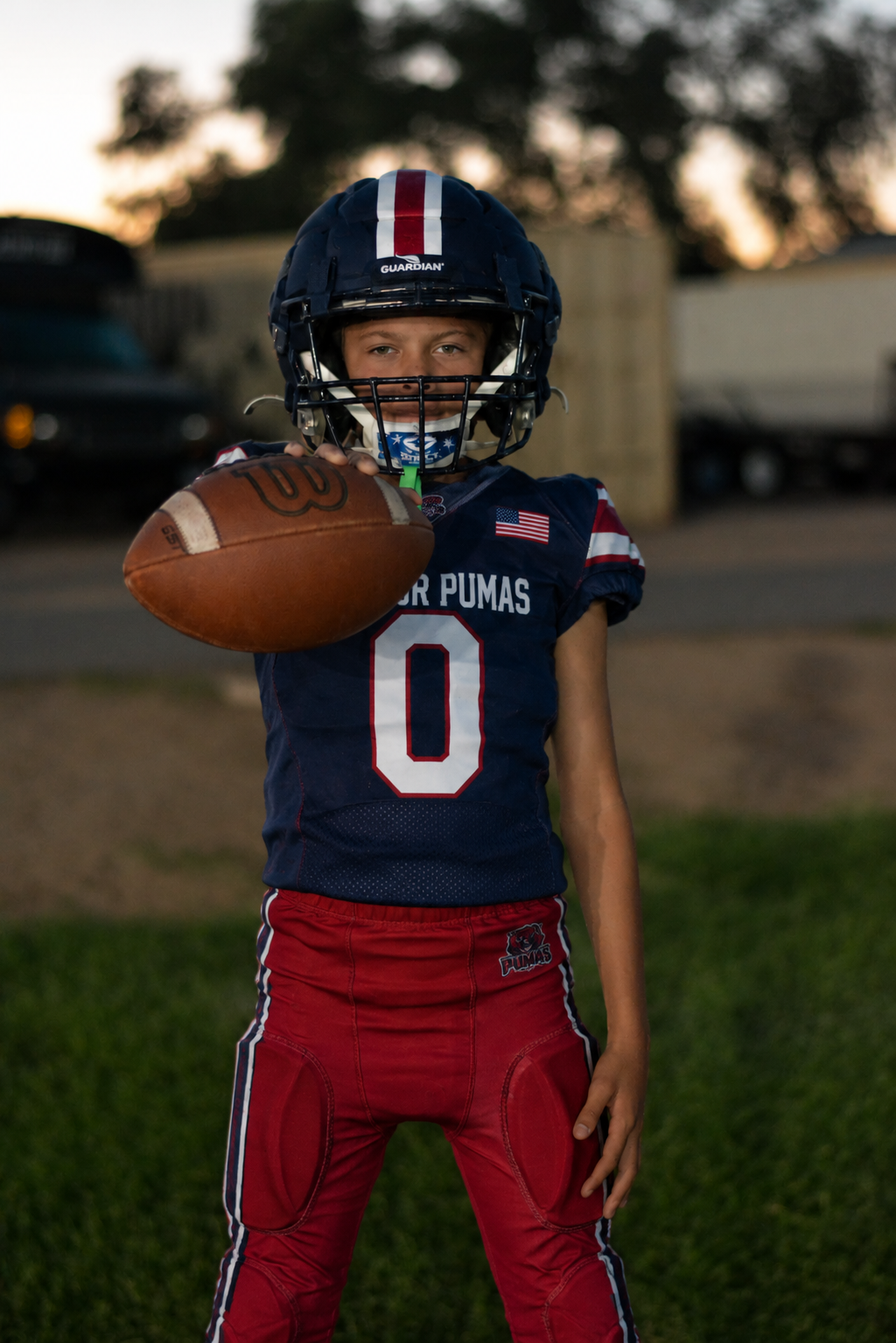 Football player holding a football on a green field at a stadium at night.