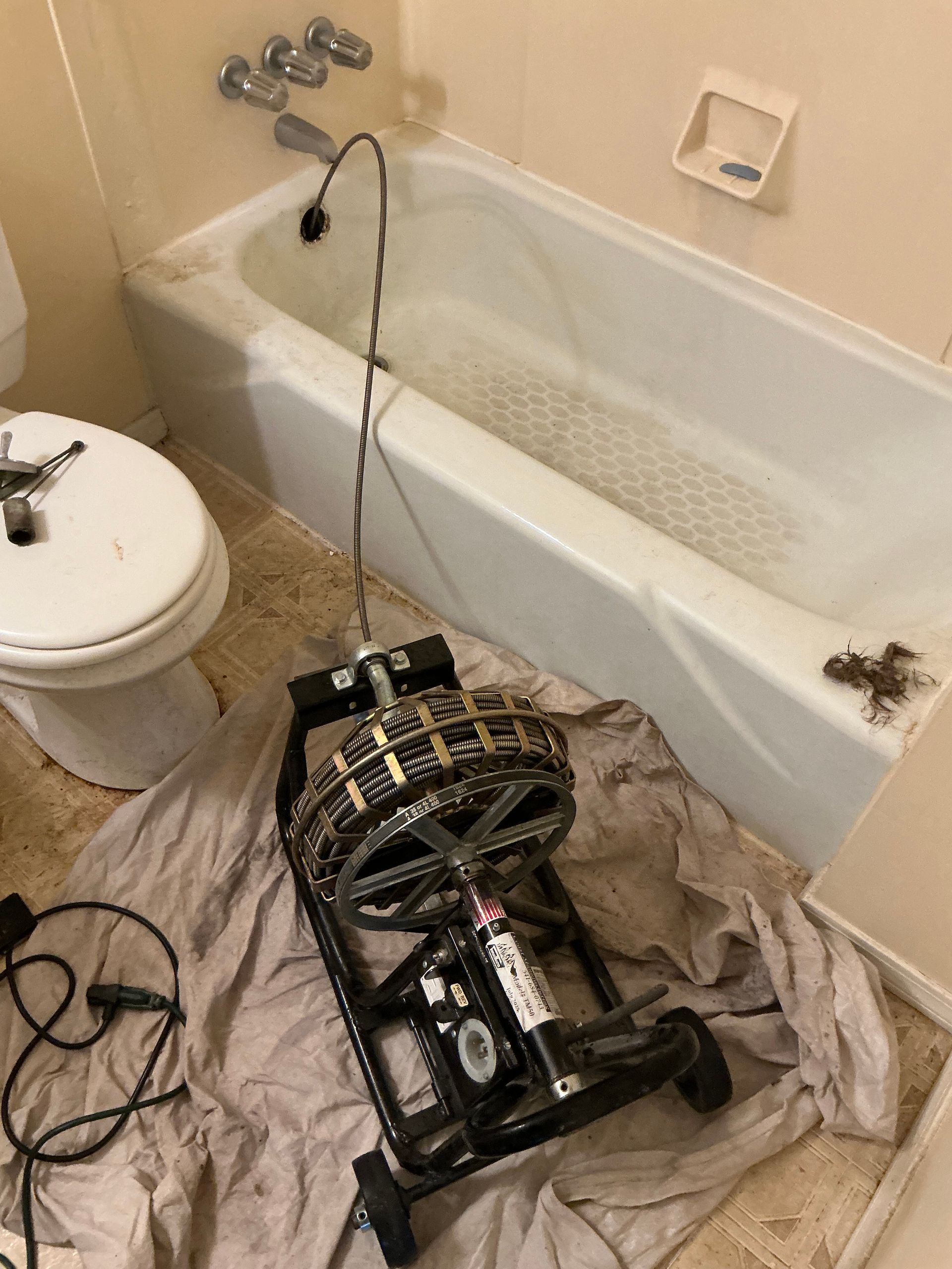 A plumbing snake machine sits in a bathroom. A tub and toilet are visible.