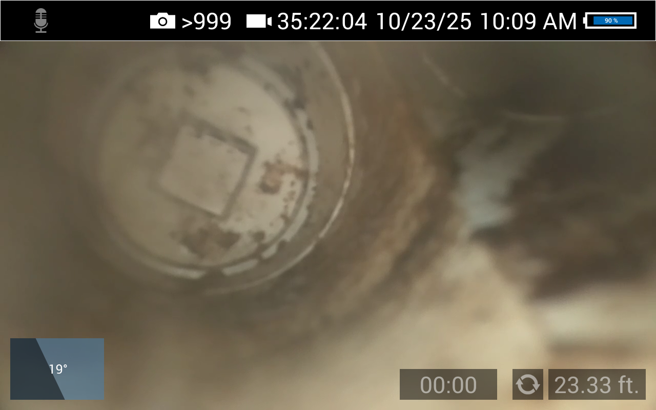 Inspection camera view inside a pipe. A square shape is visible within a circular structure. Debris and discoloration are present.
