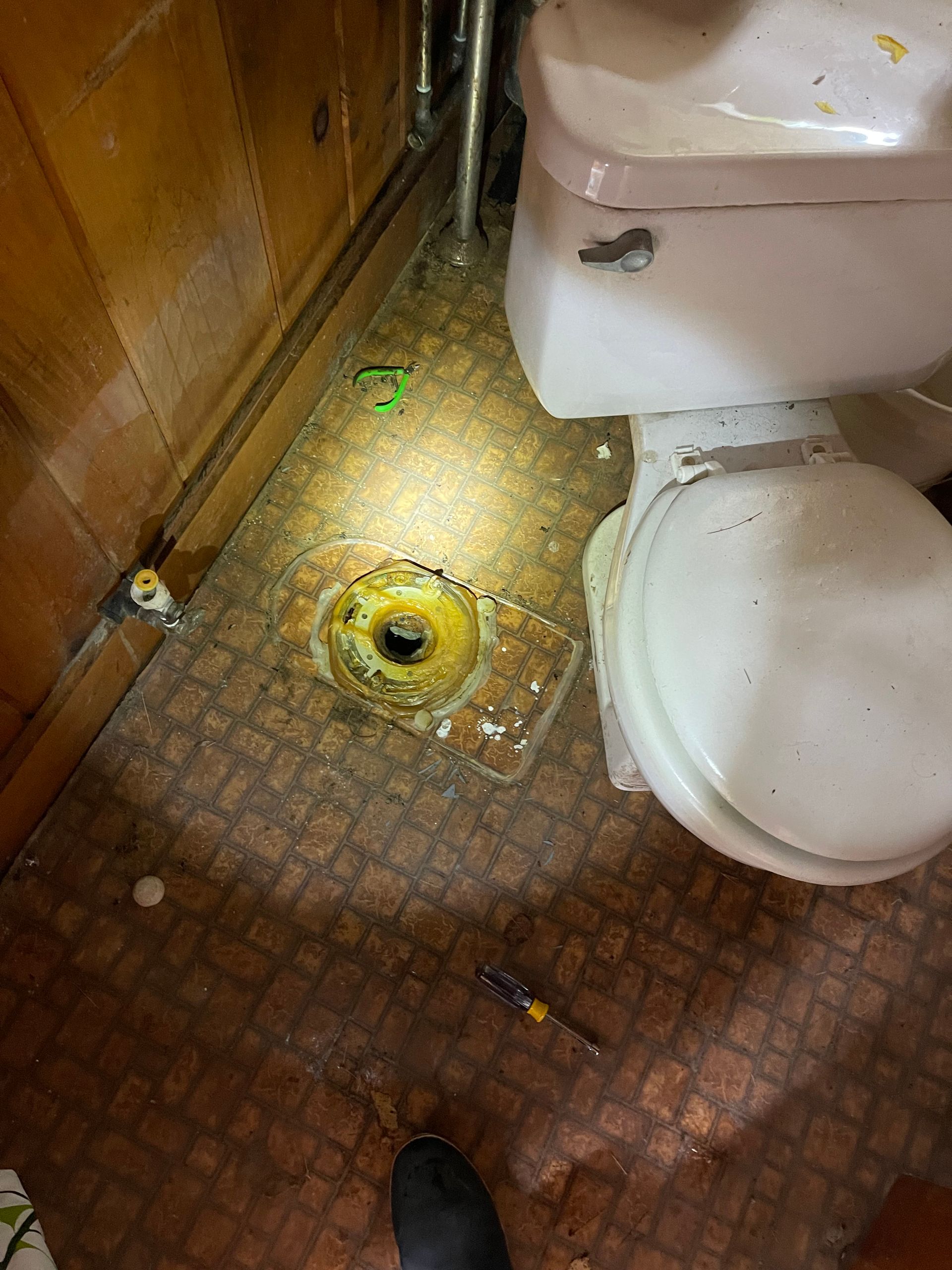 Toilet base removed, showing drain on brown patterned floor, with a tool nearby.