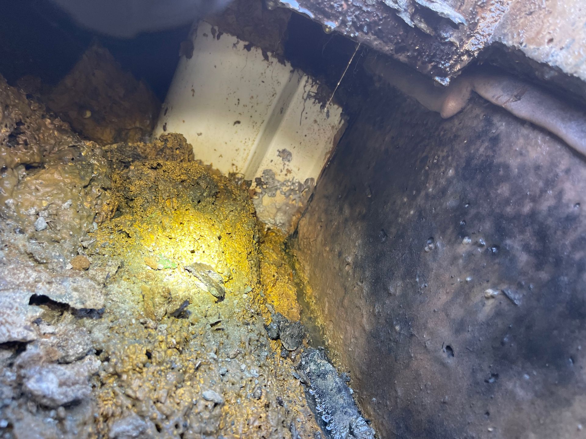 A close-up view of a crumbling brick structure with a white PVC pipe visible. Yellow-brown soil surrounds the pipe.