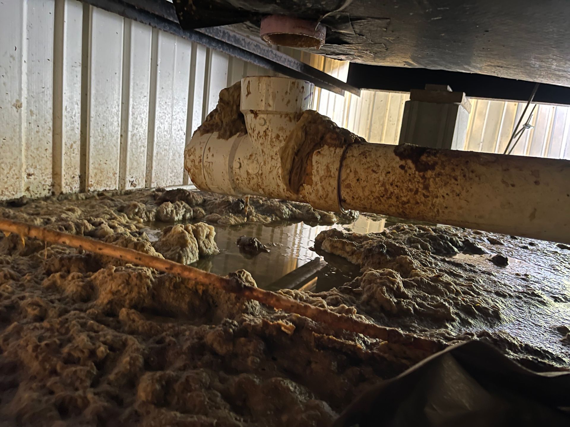 Overflowing sewage under a structure, with a broken white pipe and a mass of brown sludge.