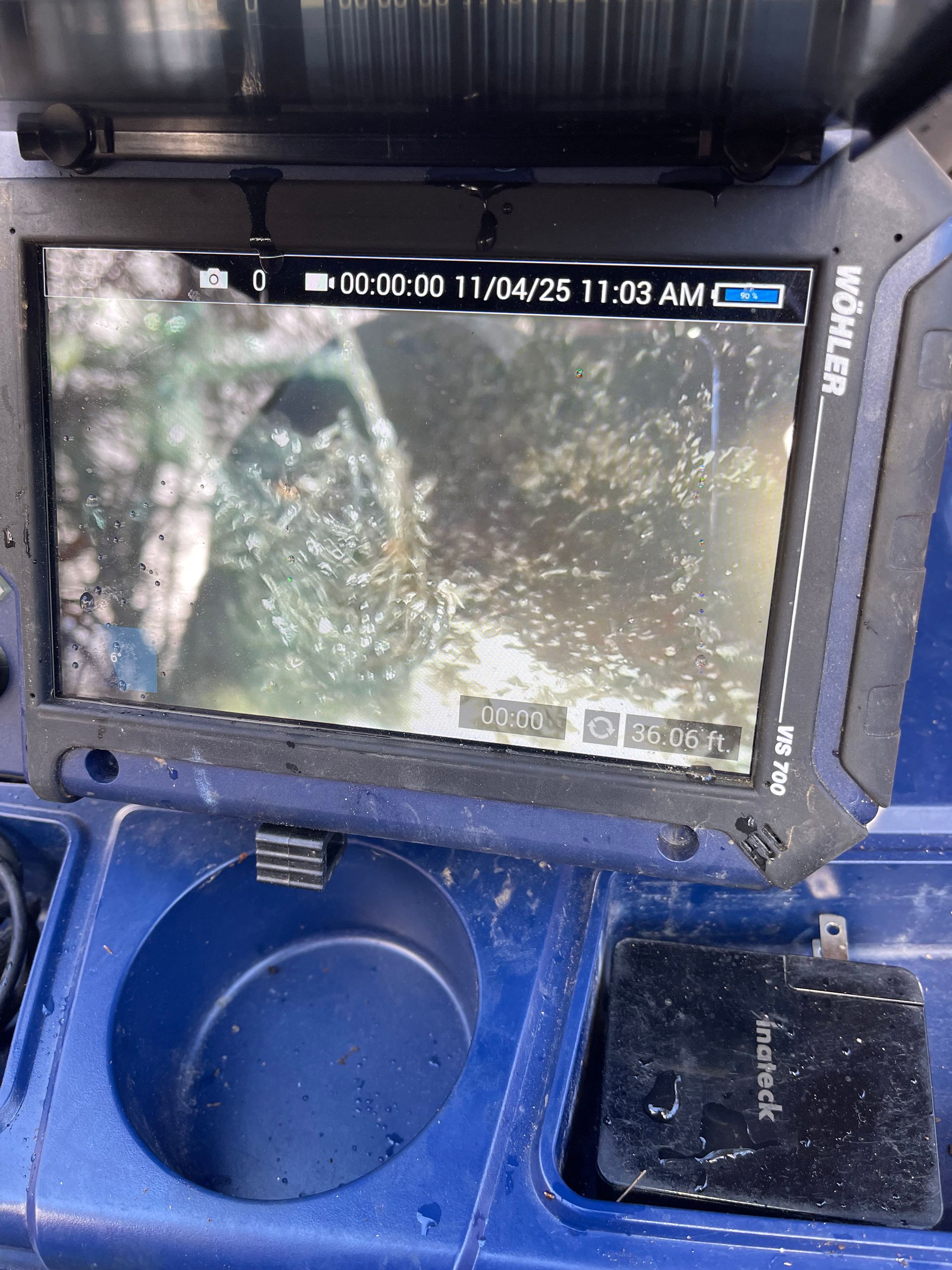 Screen displaying a blurry view of foliage captured by a camera; the screen is mounted on a blue utility tool.