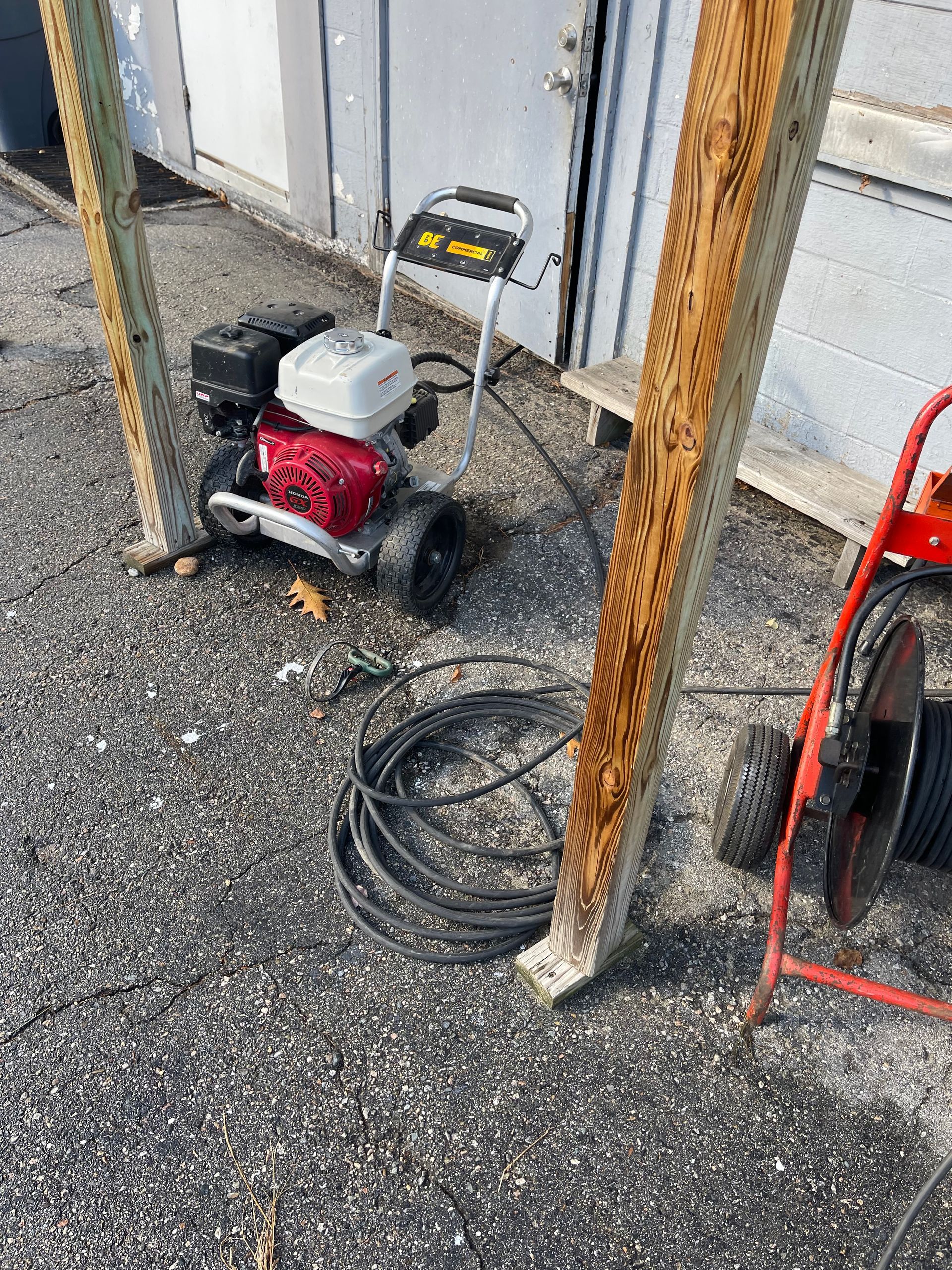Pressure washer and equipment next to wooden posts on gravel.