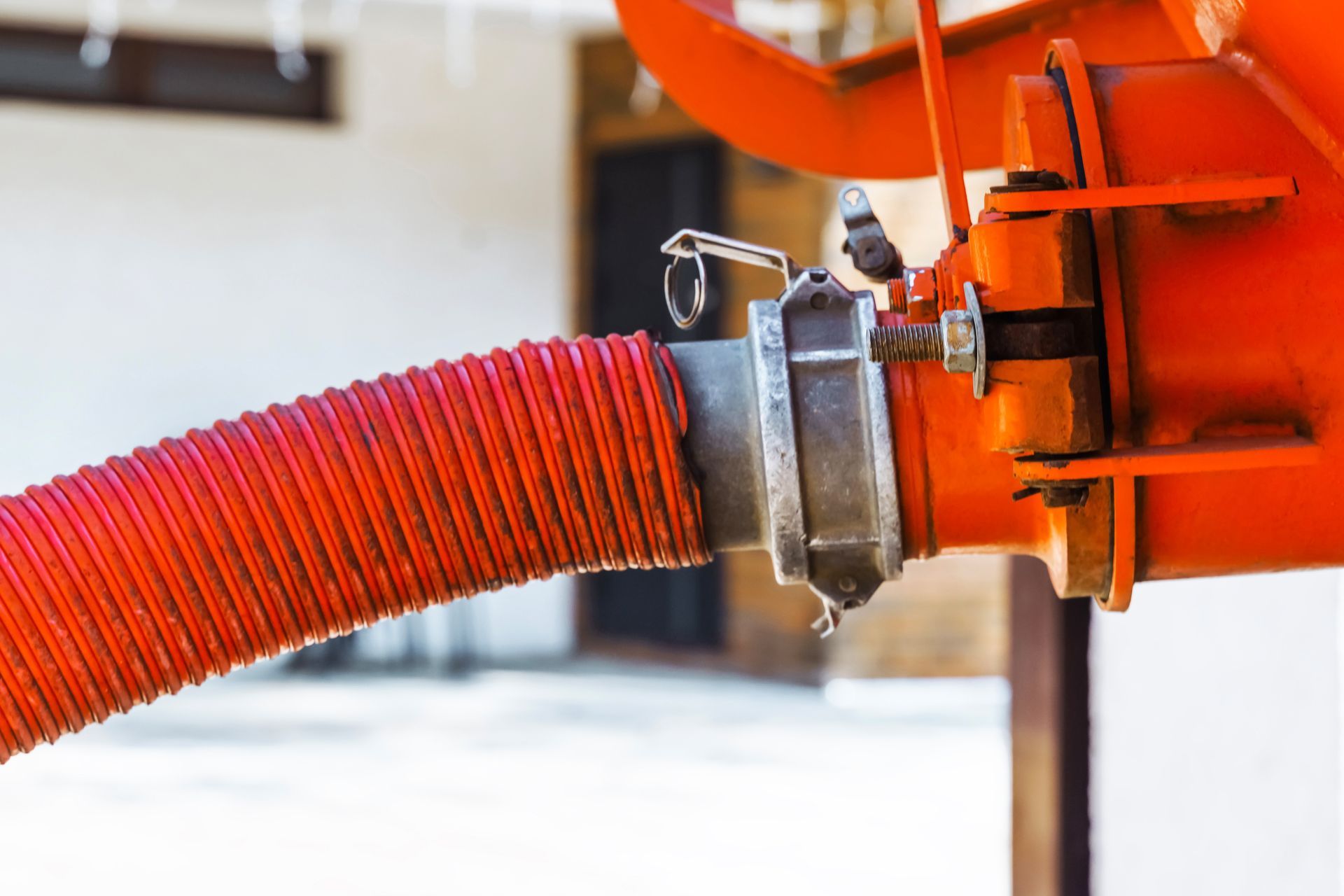 Close-up of a red hose connected to orange machinery with a metal clasp.