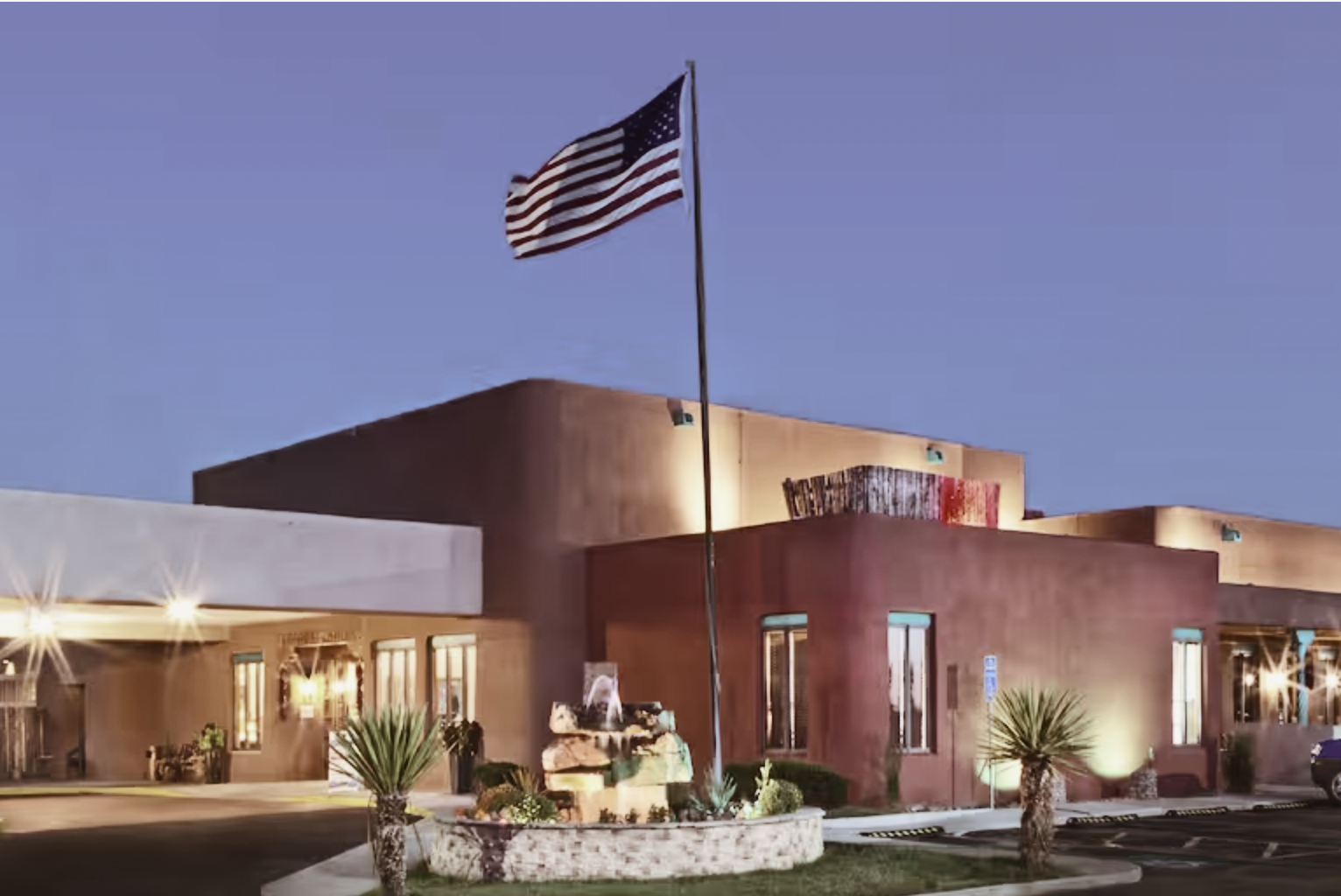 An exterior image of the Hotel Don Fernando in the evening with lights on and an American flag flying.