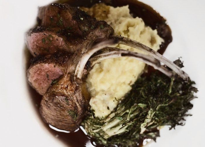 Rack of lamb, mashed potatoes and sautéed greens on a white plate.