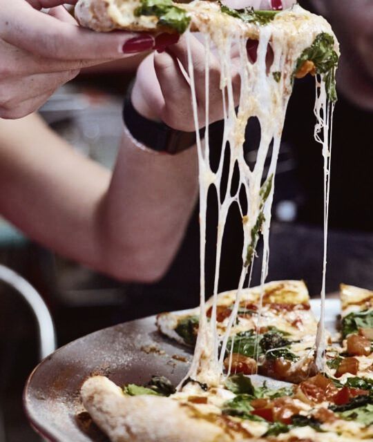 A person raising a pizza slice of a pizza with mozzarella cheese being pulled.