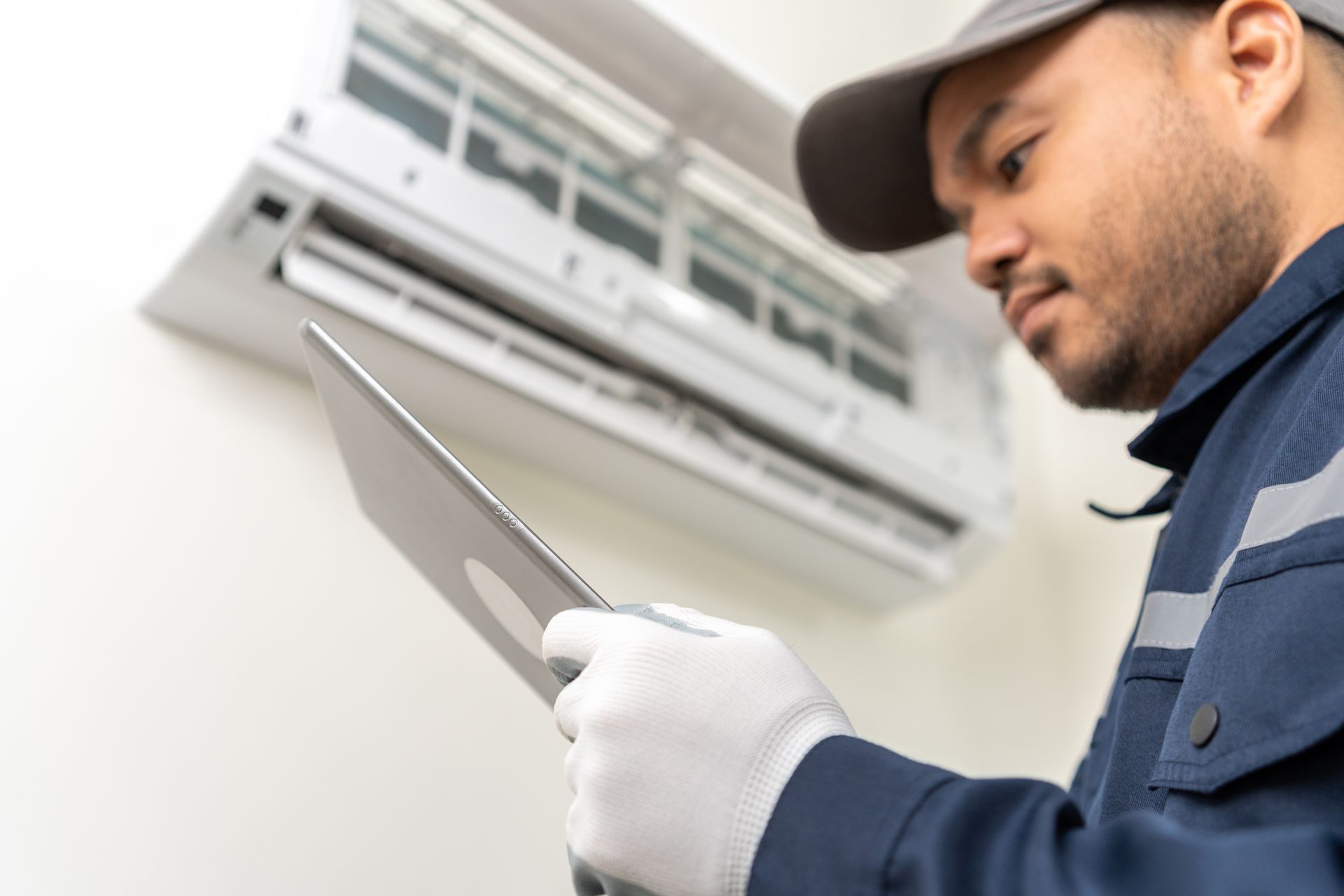 HVAC technician checking a wall-mounted AC unit with a tablet.