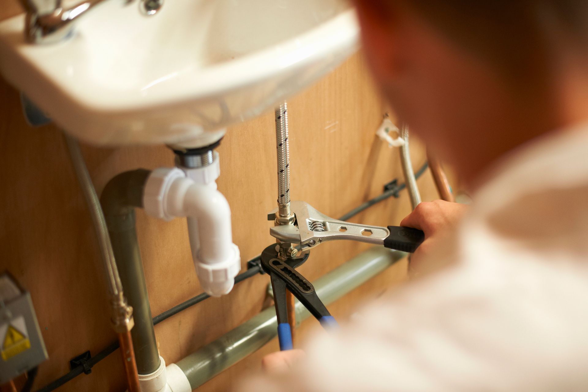 Plumber fixing a pipe under a white sink with a wrench in a bathroom.