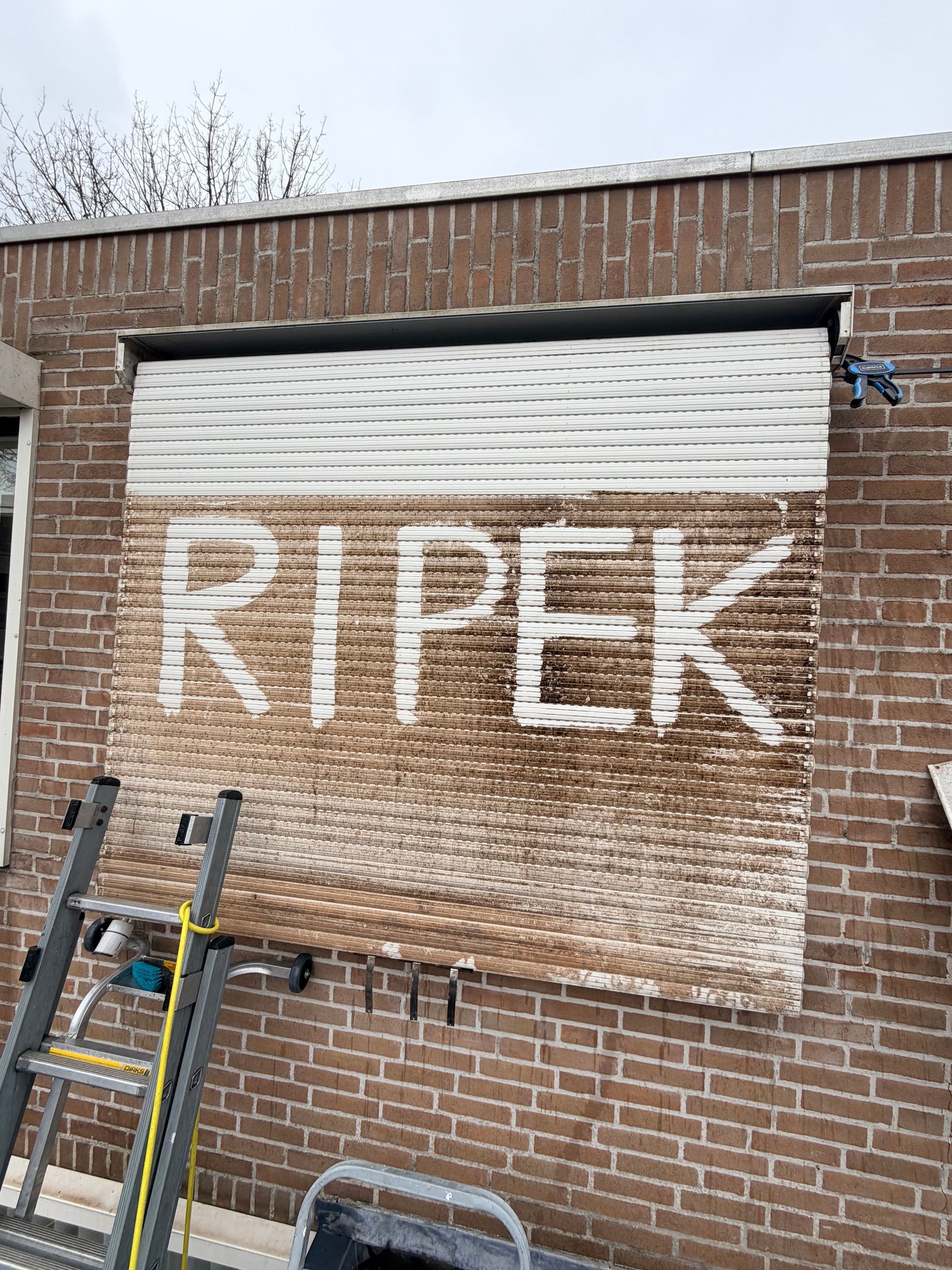 Iemand die met een borstel aan een slang een rolluik schoonmaakt.