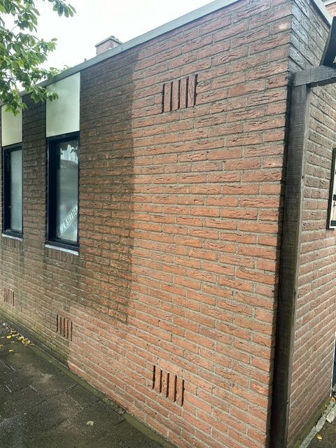Buitenzijde van een bakstenen gebouw met ramen en ventilatiesleuven, bruine bakstenen, grijze afwerking.