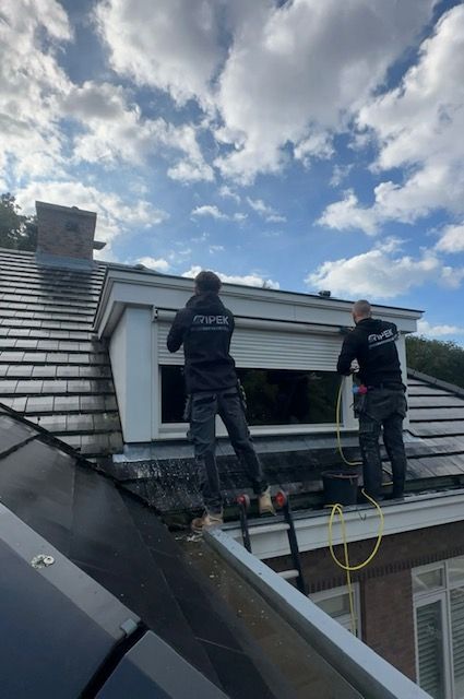 Twee arbeiders installeren een rolluik voor een raam in een schuin dak. Bewolkte lucht.