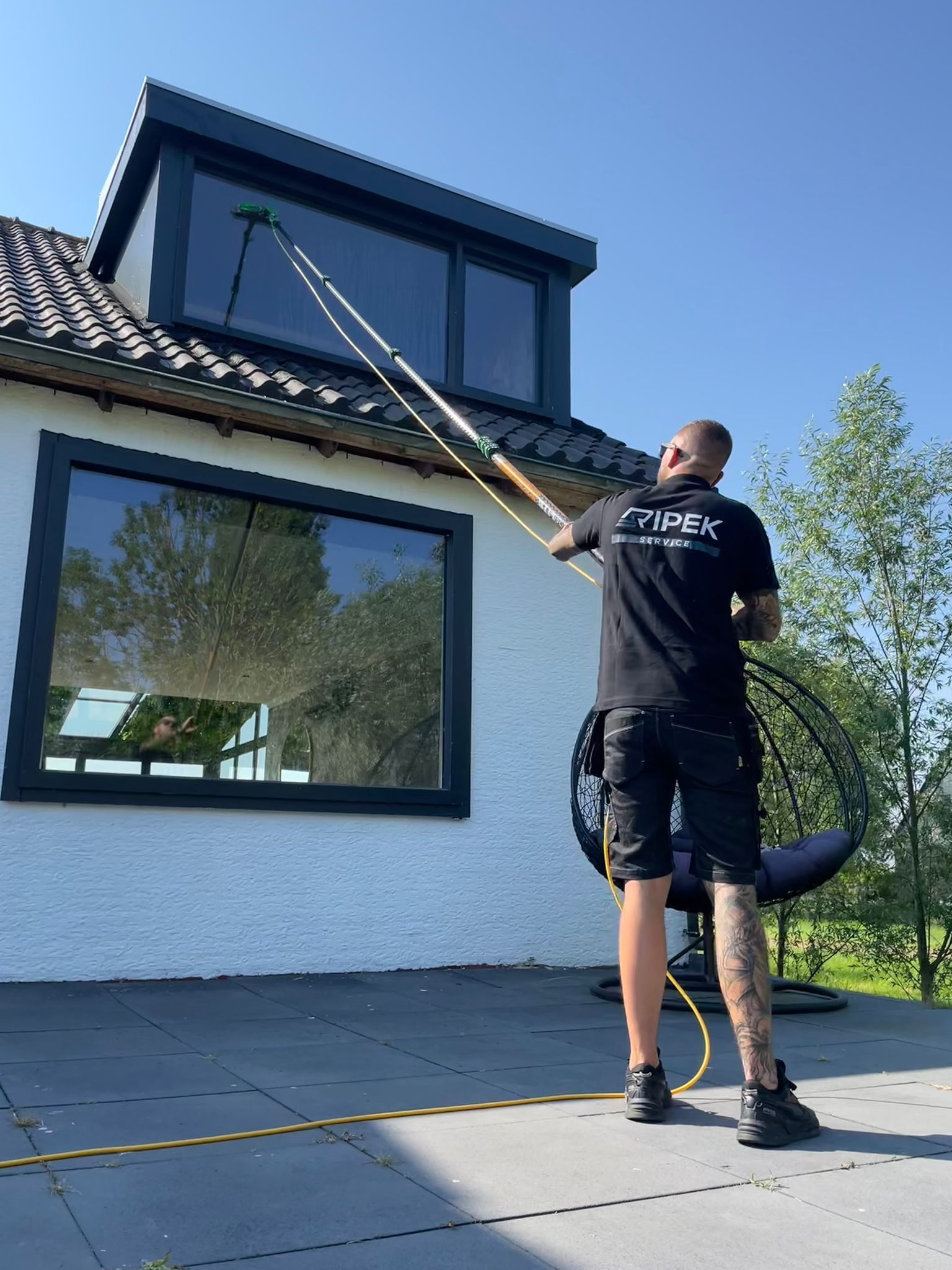 Een man maakt de ramen van een huis schoon met een borstel met lange steel, op een zonnige dag.