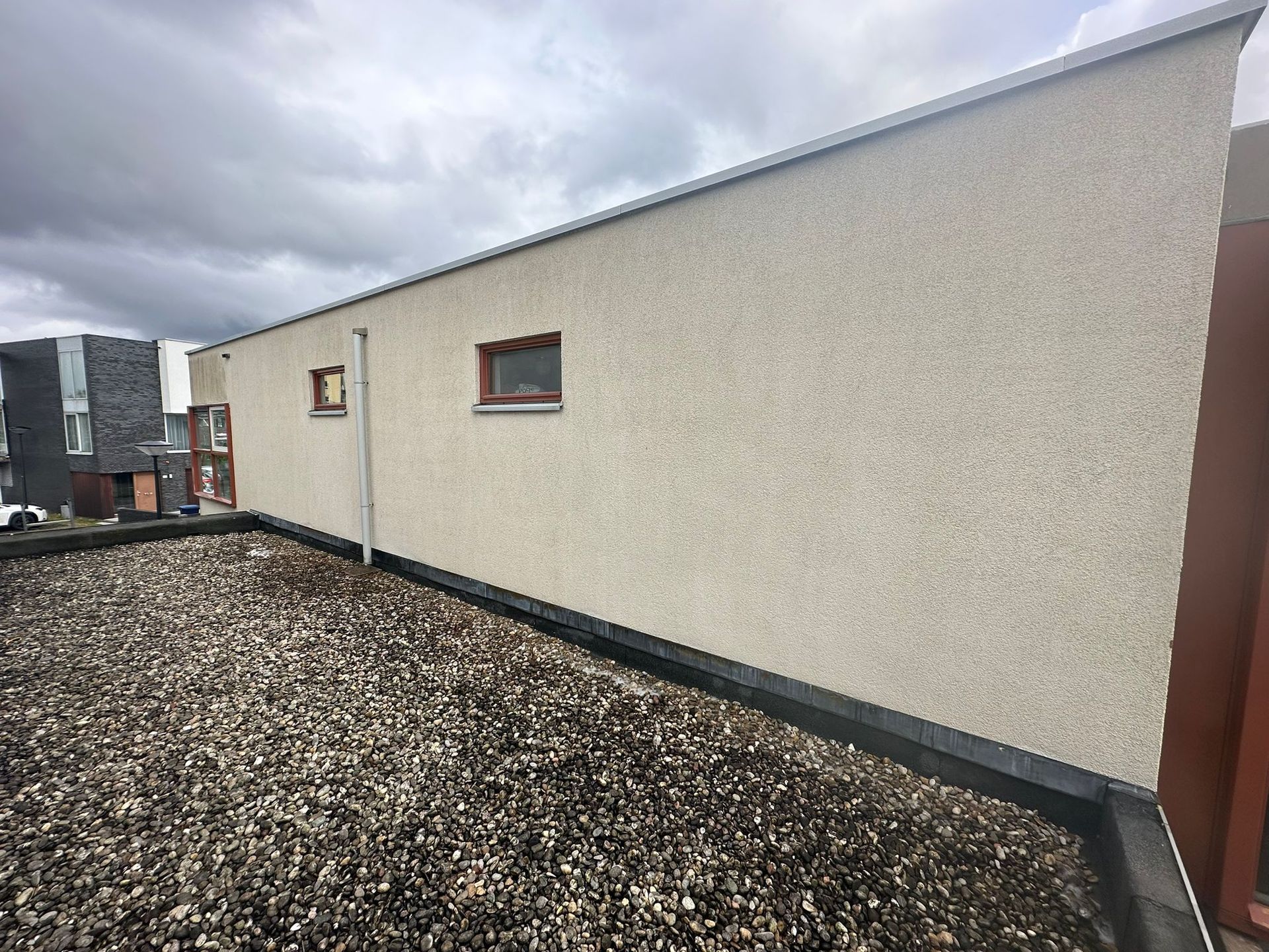 Zijaanzicht van een gebouw met een plat, met grind bedekt dak en lichtbeige muren met een structuurafwerking.