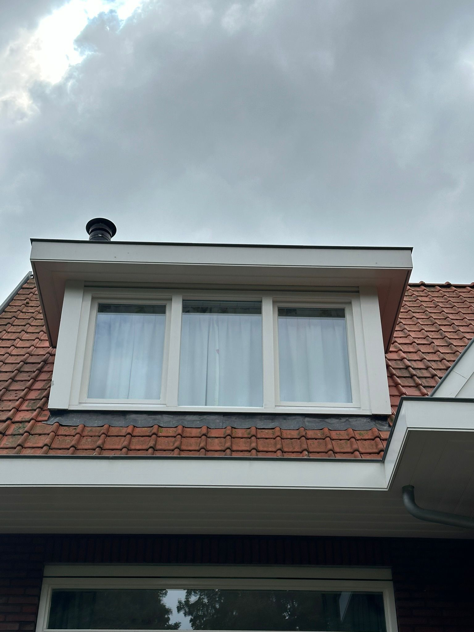 Dakkapel met drie ruiten in een rood pannendak onder een bewolkte hemel.