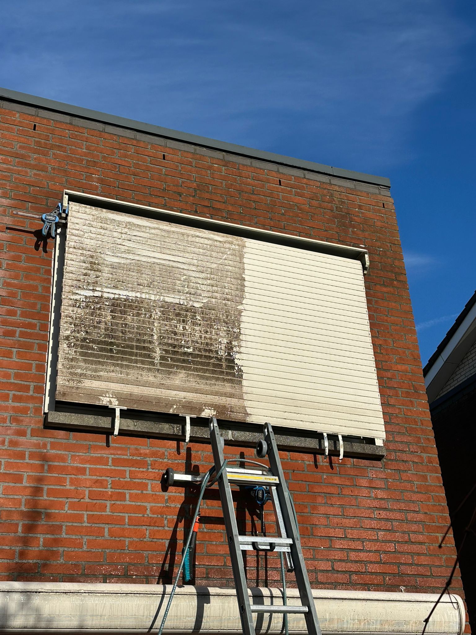 Een ladder die tegen een bakstenen muur leunt, waarmee een afgedekt raam of uithangbord onder een blauwe hemel wordt bereikt.