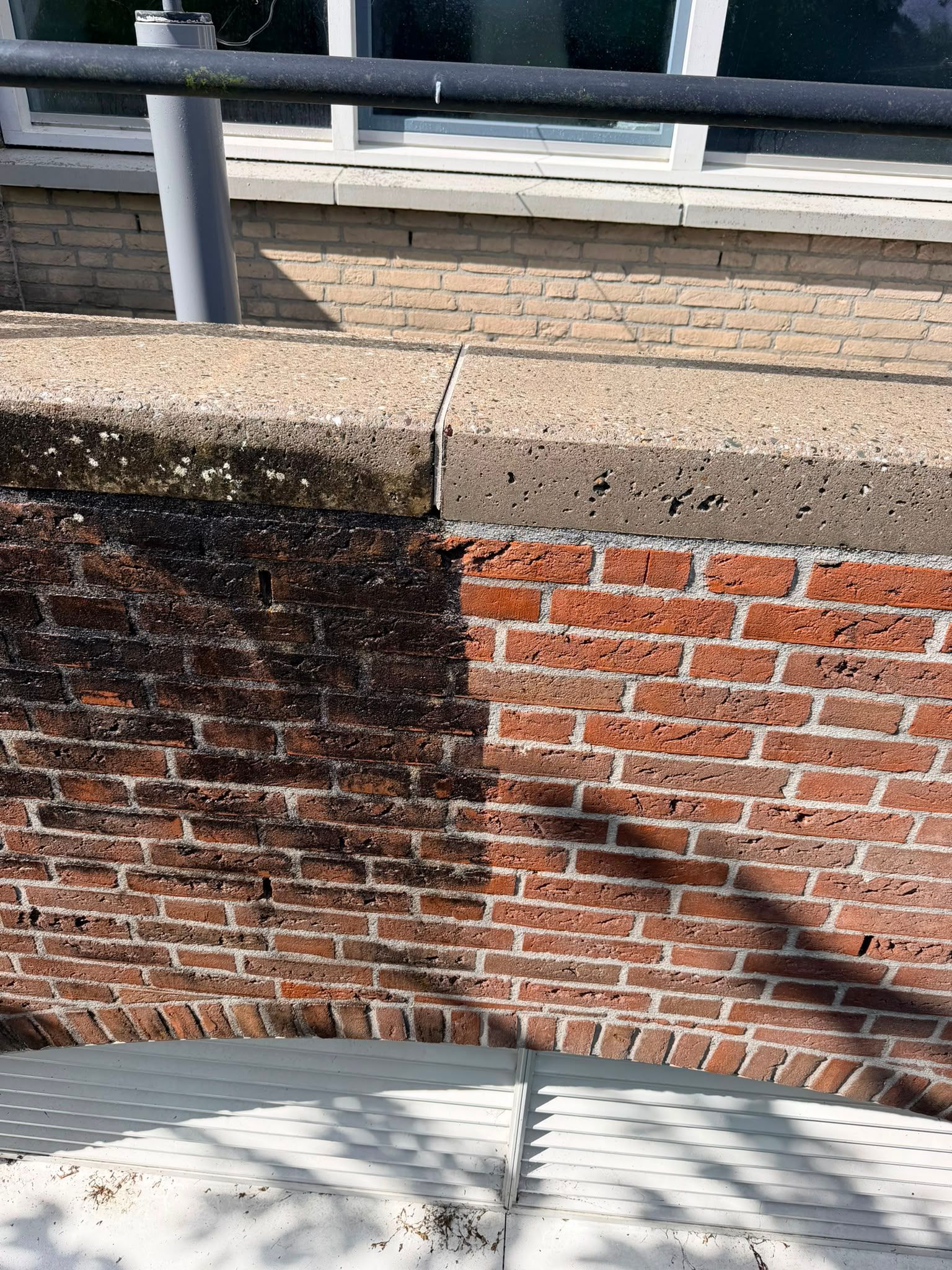 Een bakstenen keermuur met een donkere beits, een betonnen bovenzijde en een metalen reling erboven.
