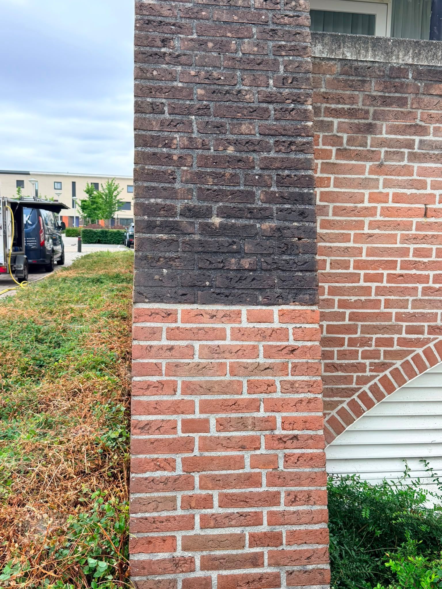 Hoek van een bakstenen gebouw met donkere, opgevulde reparatieplekken boven rode bakstenen en witte gevelbekleding eronder.