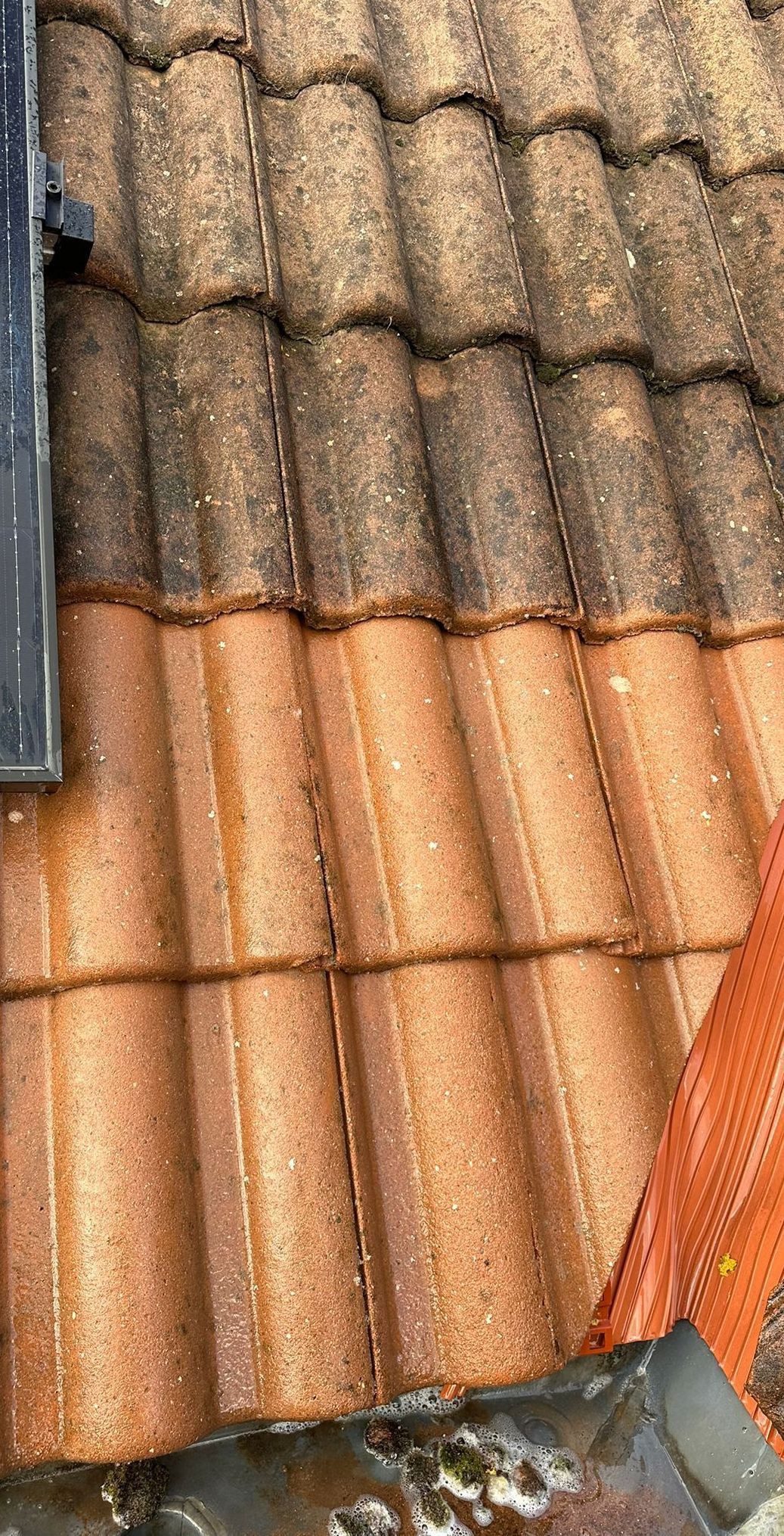 Close-up van een terracotta dak, waarbij sommige dakpannen donkerder en vuiler lijken dan de nieuwere, schonere pannen eronder.