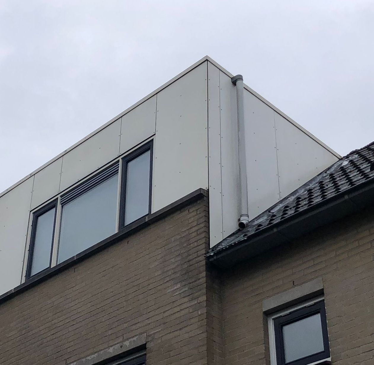 Modern gebouw met witte gevelbekleding op de bovenverdieping, baksteen eronder en ramen.