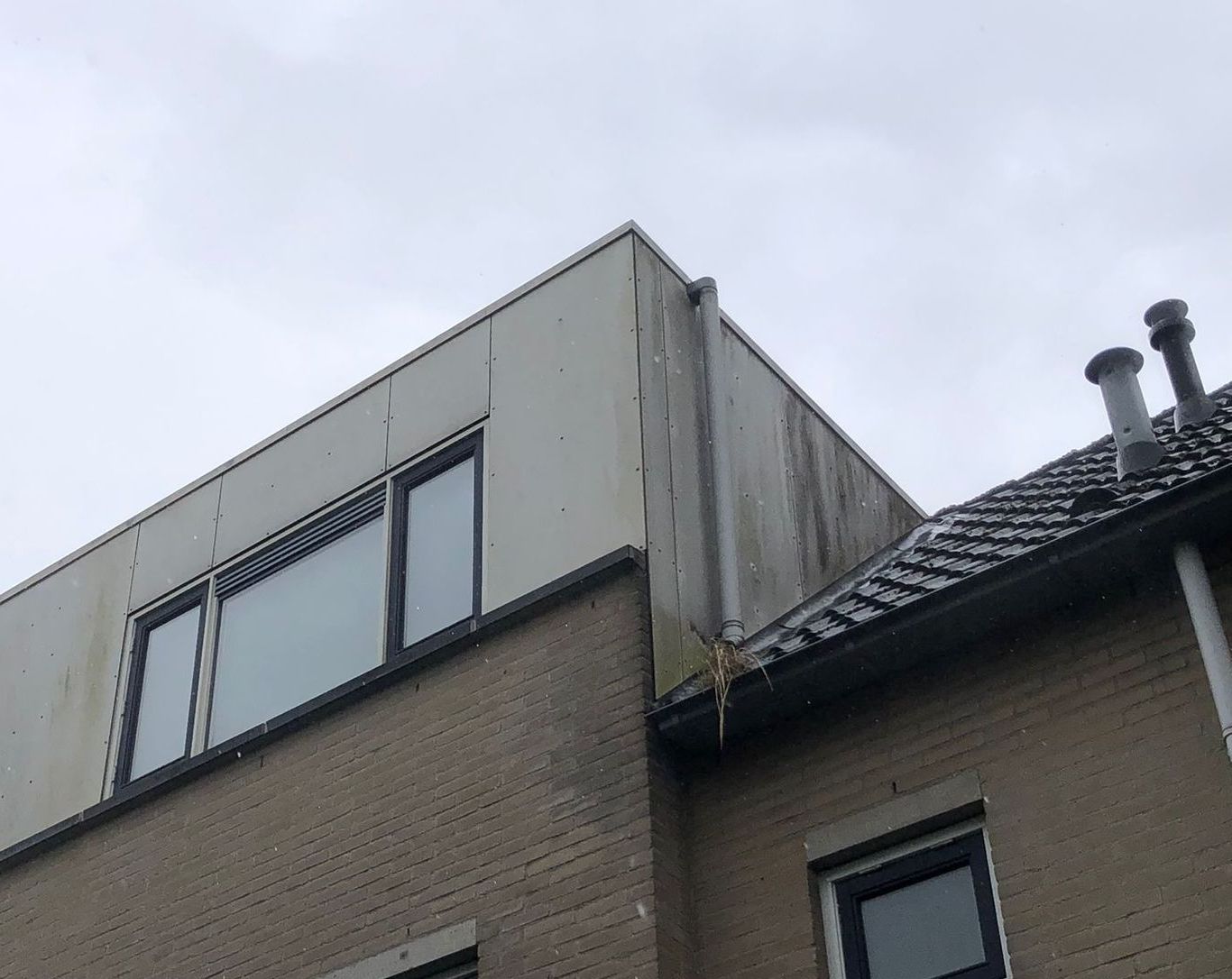 Buitenkant van een gebouw met een plat dak en een bakstenen gevel; grijze lucht erboven.