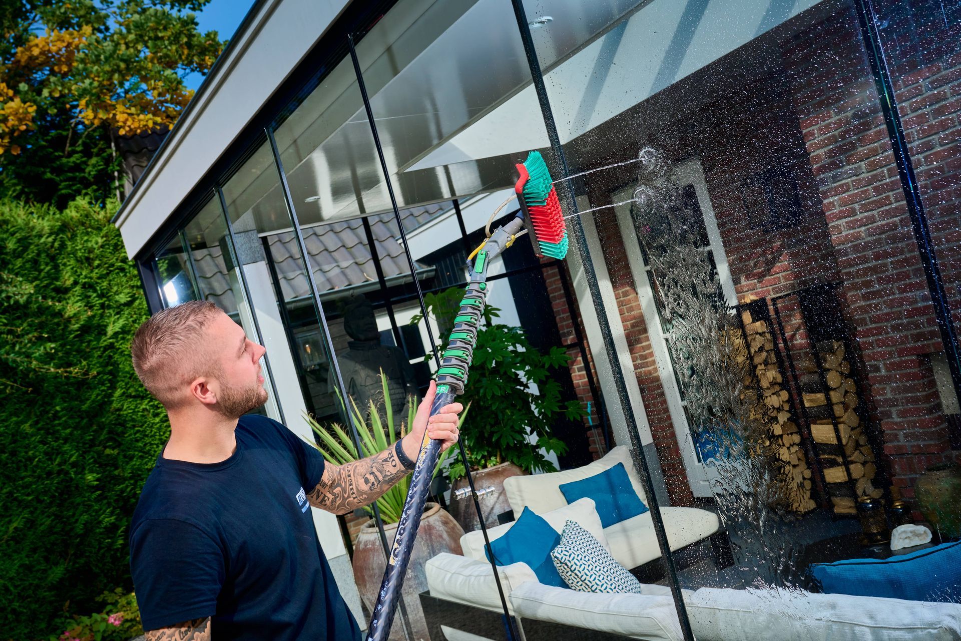 Een man wast een raam met een schoonmaakgereedschap, buiten.