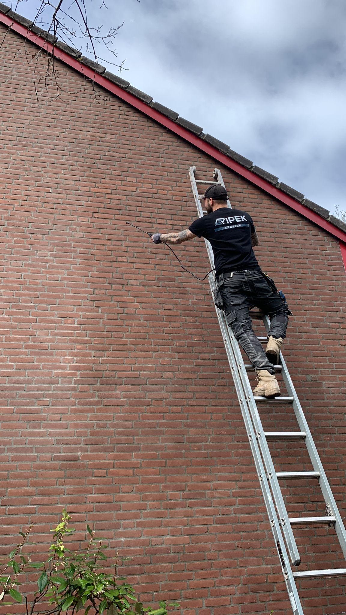 Een man staat op een ladder tegen een bakstenen muur en werkt aan de zijkant van een gebouw.