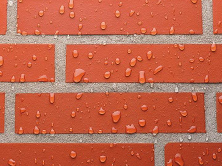 Close-up van een bakstenen muur met waterdruppels op de rode bakstenen en grijze mortel.