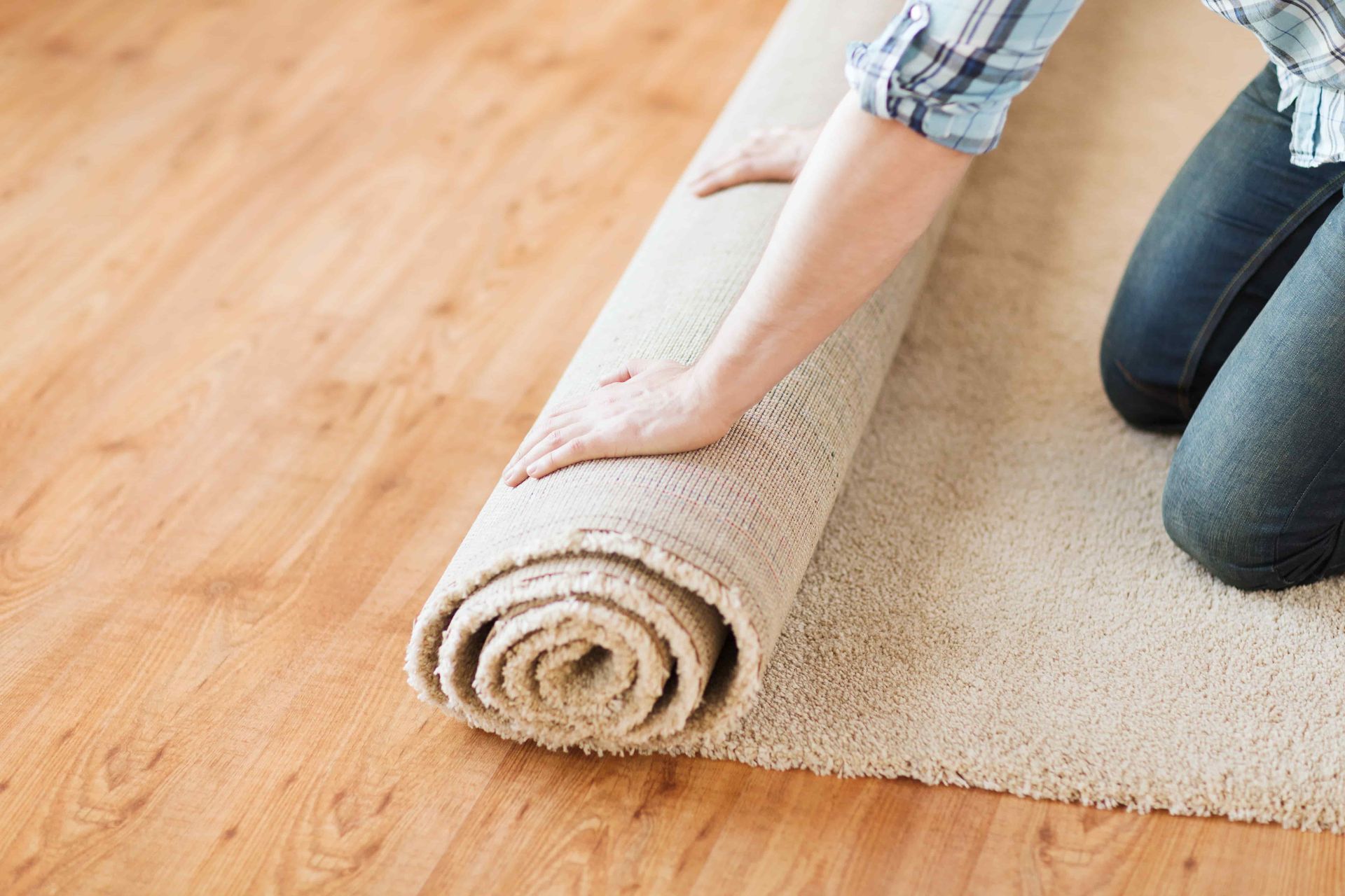 A person is rolling a rug on a wooden floor.