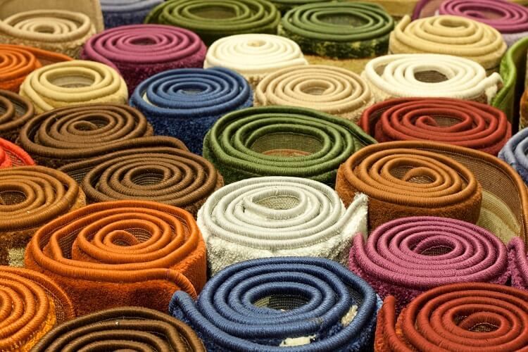A bunch of rolls of different colored rugs are stacked on top of each other.