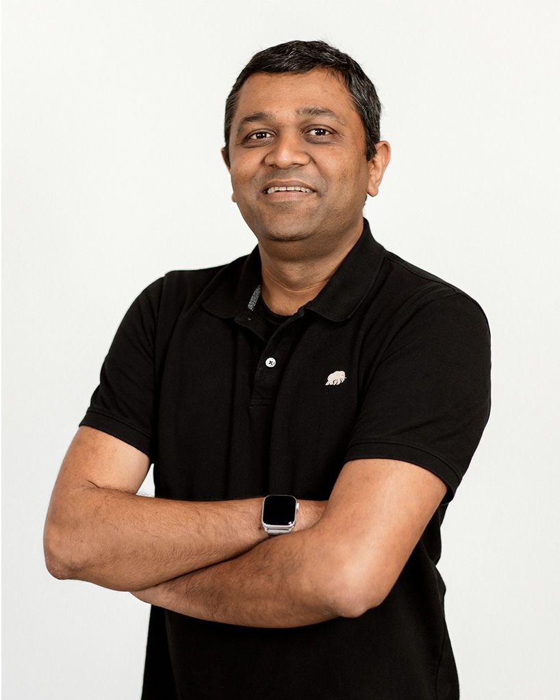 Smiling man in a black polo shirt, standing with arms crossed against a white background
