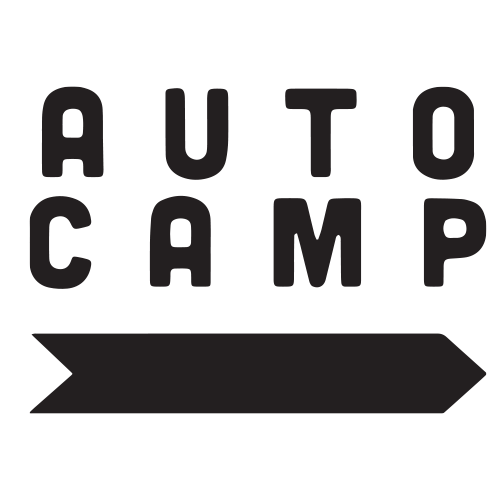 A black and white logo for auto camp with an arrow pointing to the right.
