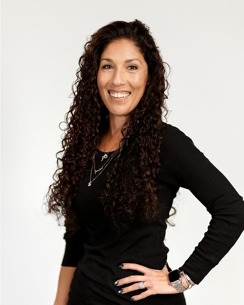 Smiling woman in black top with hand on hip against a white background