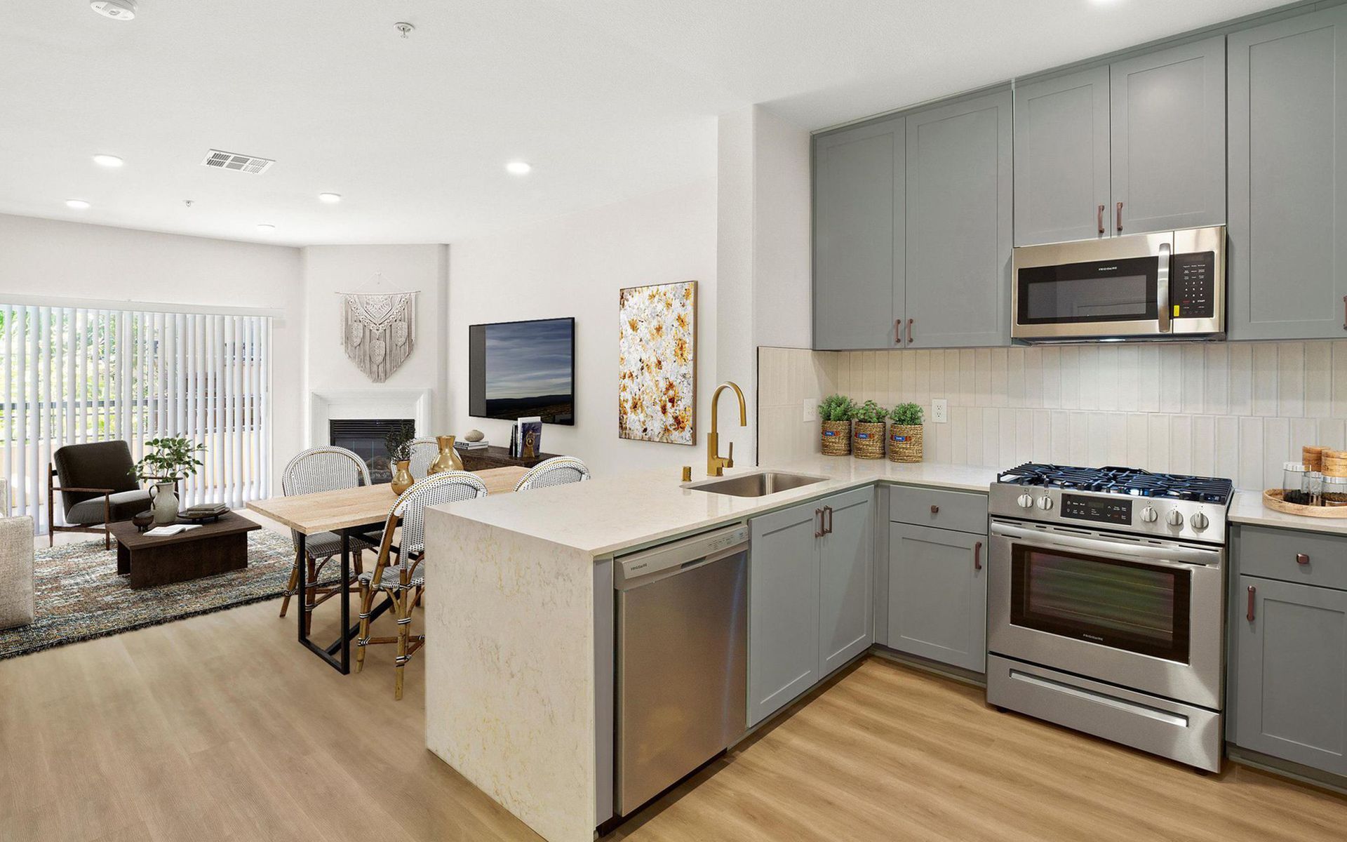 Modern open-plan kitchen and living room with gray cabinets, stainless appliances, and light wood flooring