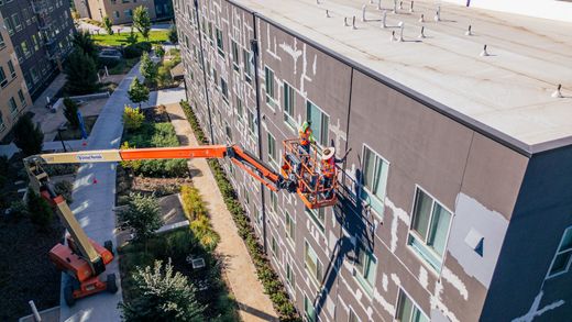 Workers in orange lifts repairing a building wall along a city street