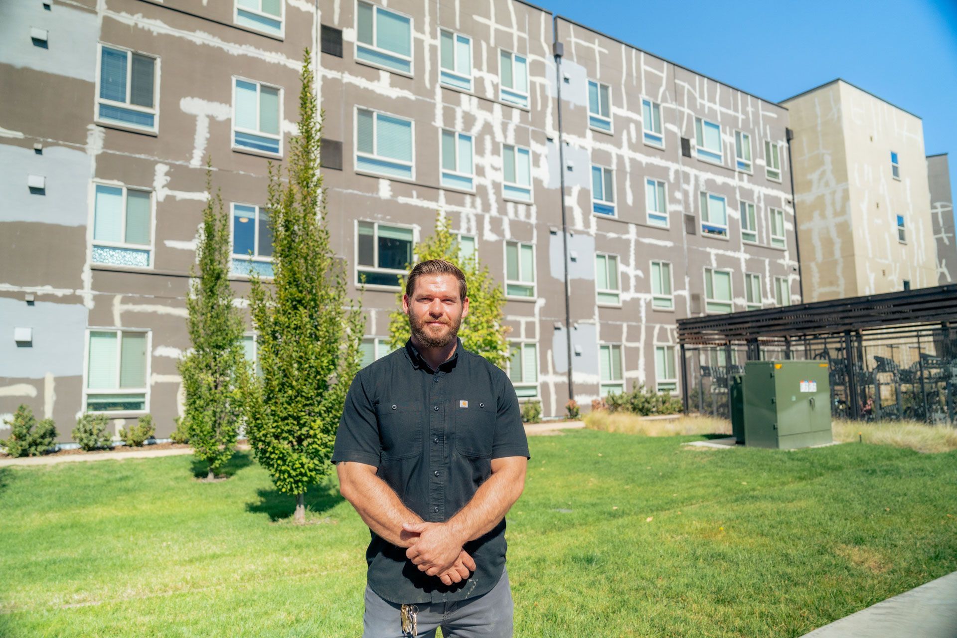 Man standing on grass in front of a modern apartment building on a sunny day