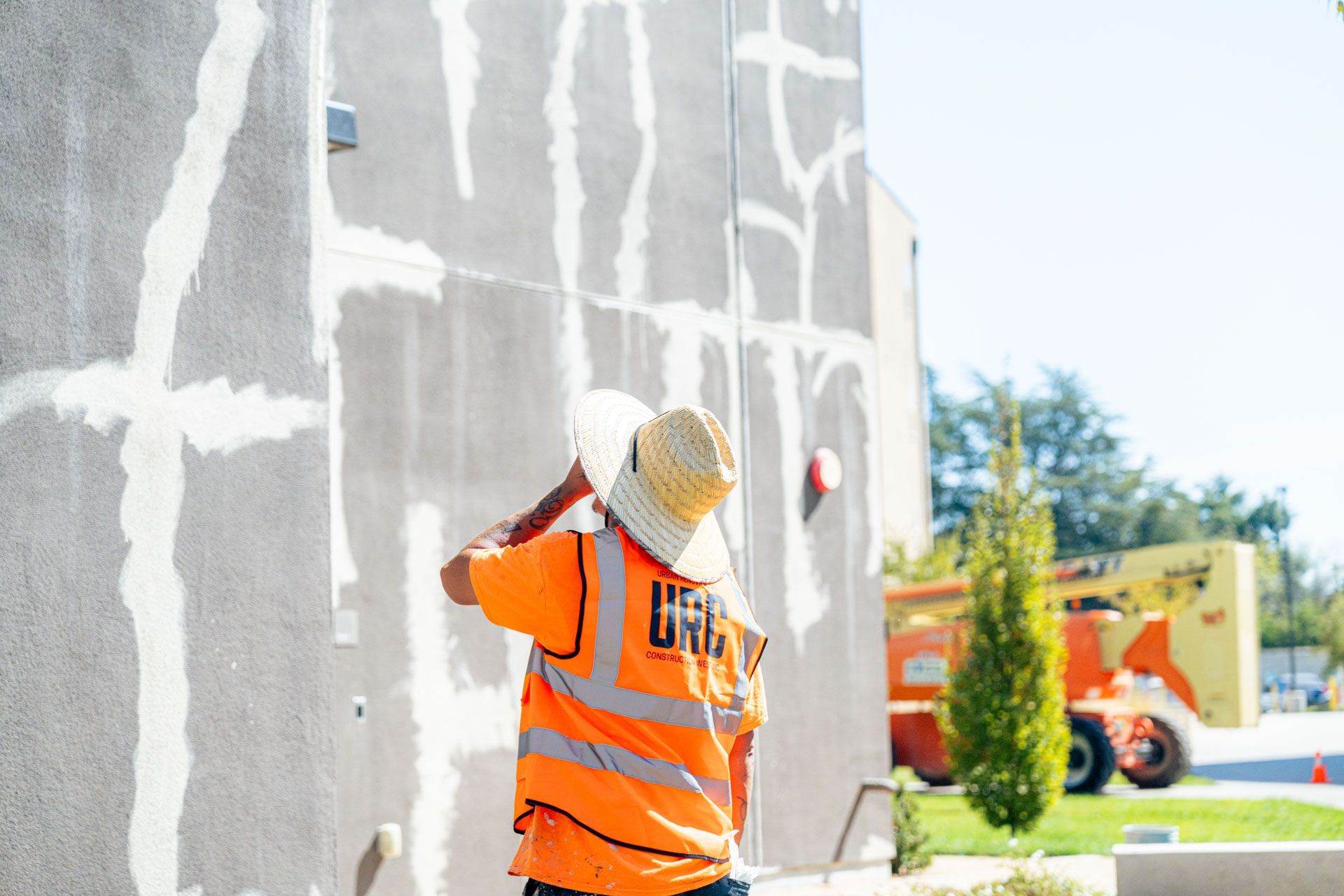 Construction worker in orange safety vest painting a gray wall outdoors