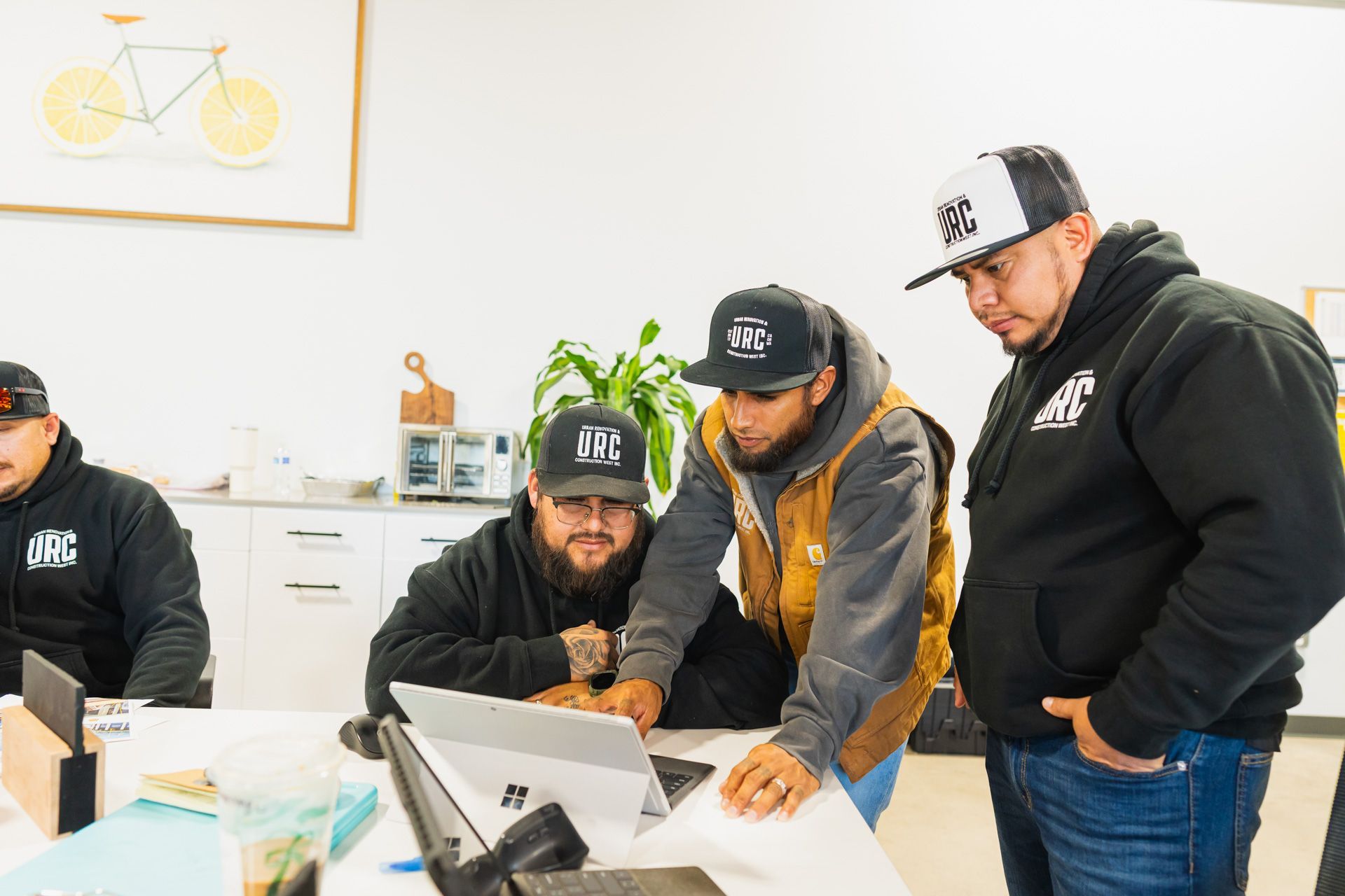 Four URC employees lean over a laptop in a bright office, discussing something on the screen.