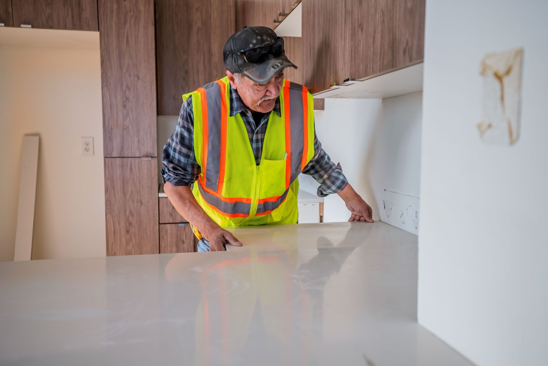 Worker in a neon safety vest inspecting a countertop in a modern kitchen under construction