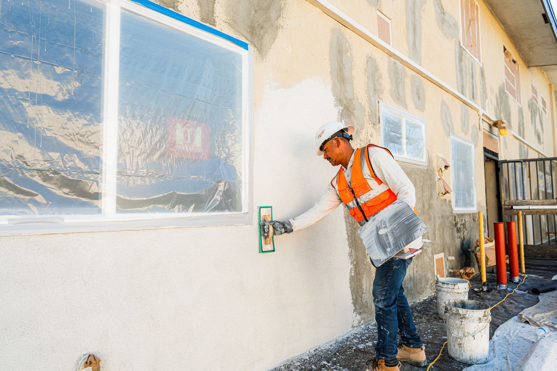 Worker in orange safety vest painting an exterior wall beside a window