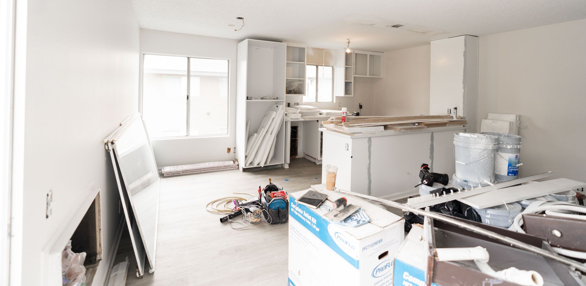 Bright unfinished kitchen and living room with tools, boxes, and renovation materials scattered around